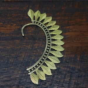 May include: Gold ear cuff with a leaf design. The cuff is curved and has a delicate, intricate pattern.