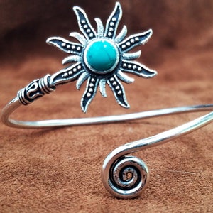 May include: Silver cuff bracelet with a turquoise sun design. The bracelet has a spiral detail at the end.
