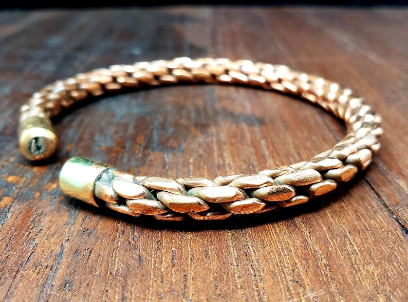 May include: A braided copper bracelet with a simple, minimalist design. The bracelet is made of a single strand of copper wire that has been braided together to create a textured look. The ends of the bracelet are secured with a simple clasp.