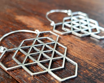 May include: A pair of silver hoop earrings with a geometric design. The design is made up of multiple hexagons that are layered on top of each other.