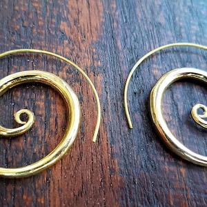 May include: A pair of gold-toned hoop earrings with a spiral design. The earrings are made of metal and have a simple, elegant look.