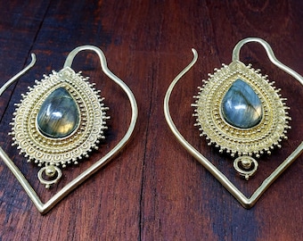 May include: A pair of ornate gold-colored earrings. Each earring features a teardrop-shaped, iridescent gemstone set within a detailed, circular frame. The earrings have a unique, openwork design with a curved, heart-like shape.