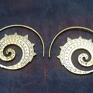 May include: A pair of gold-toned hoop earrings with a spiral design. The earrings are made of metal and have a delicate, intricate pattern.