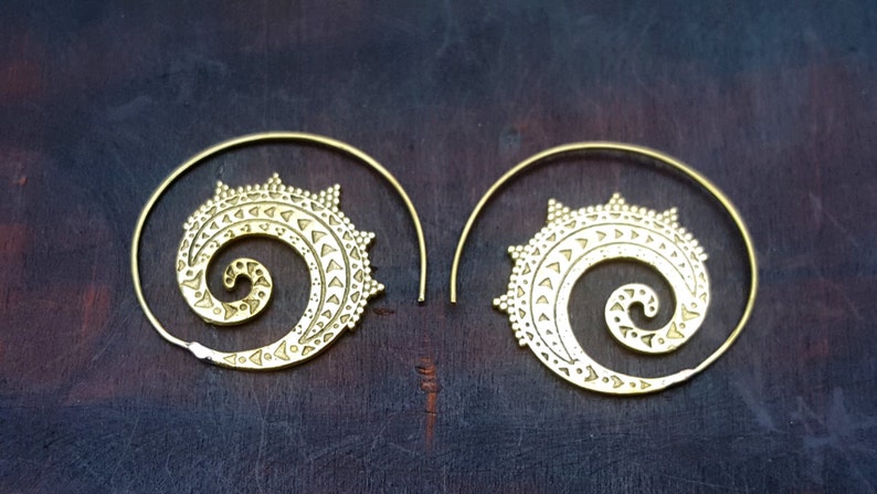 May include: A pair of gold-toned hoop earrings with a spiral design. The earrings are made of metal and have a delicate, intricate pattern.