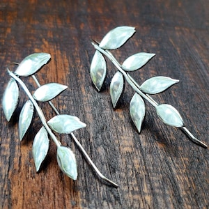 May include: A pair of silver earrings shaped like a branch with leaves. The earrings are delicate and have a hammered texture.