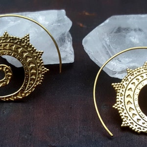 May include: A pair of gold-toned spiral hoop earrings with a detailed, intricate design. The earrings are made of metal and have a circular shape.