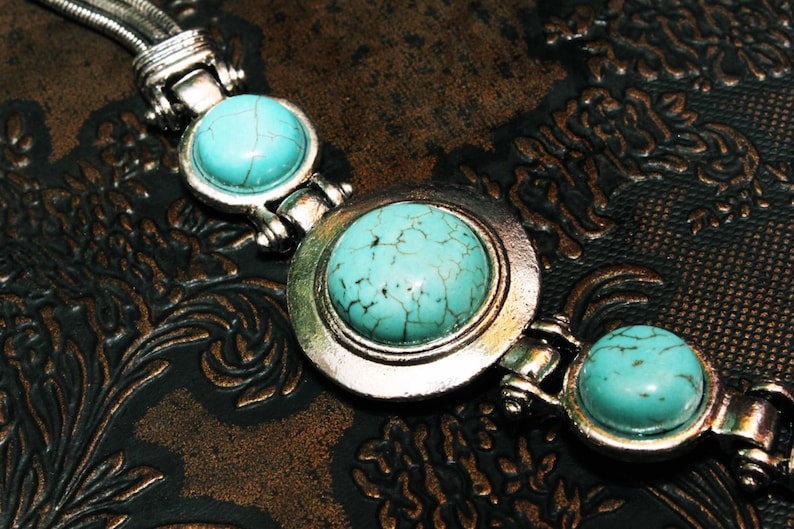 May include: A silver bracelet with three turquoise stones. The stones are set in silver bezels and the bracelet has a chain link design.
