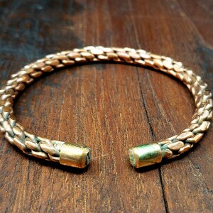 May include: A copper bracelet with a braided design and gold-toned end caps.