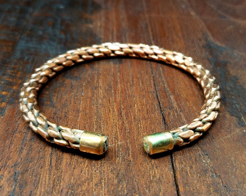 May include: A copper bracelet with a braided design and gold-toned end caps.