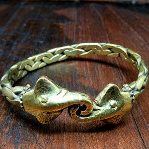 May include: A gold-toned bracelet with two elephant heads facing each other. The bracelet is made of a braided metal chain.