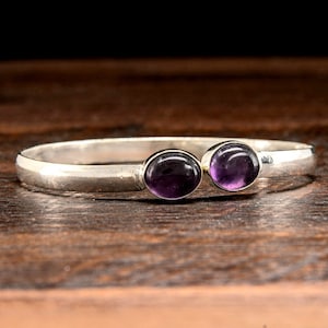 May include: A silver bangle bracelet with two purple amethyst stones.