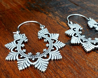 Peut inclure: Une paire de boucles d'oreilles créoles en argent avec un design détaillé et complexe. Les boucles d'oreilles sont en métal et ont une forme circulaire avec un motif floral.