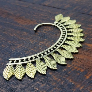 May include: Gold ear cuff with a leaf design. The cuff is made of metal and has a curved shape.