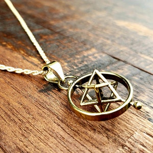May include: A gold-toned necklace with a spinning pendant featuring a geometric design. The pendant is a sphere with a Star of David inside.