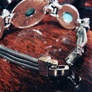May include: A silver bracelet with three strands of chain and two round turquoise-colored stones. The bracelet has a clasp closure.