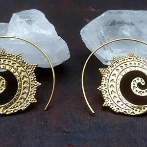May include: A pair of gold-toned spiral hoop earrings with a detailed mandala design. The earrings are made of brass and have a delicate, intricate pattern.