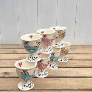 May include: A set of six ceramic egg cups with a bird design. Each cup has a different name on it: Wilfred, Emilia, Chloe, Isabelle, Annabelle, and Charlie.