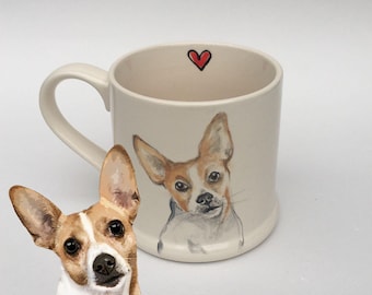 May include: A cream-coloured ceramic mug featuring a hand-painted illustration of a brown and white dog with large ears. A small red heart is painted on the interior rim. The mug is positioned next to a matching dog portrait cutout.