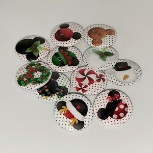 Könnte beinhalten: Eine Sammlung runder Knöpfe zum Thema Weihnachten mit verschiedenen Designs. Die Knöpfe zeigen Bilder von Mickey und Minnie Mouse, einem Lebkuchenmann, einem Schneemann, Zuckerstangen und Weihnachtskränzen. Jeder Knopf hat einen weißen Hintergrund mit roten Punkten.