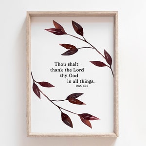May include: A framed print with a watercolor illustration of a branch with leaves in shades of brown. The print features the text "Thou shalt thank the Lord thy God in all things. D&C 59:7".