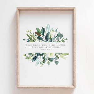 Puede incluir: Una impresi&oacute;n enmarcada con una ilustraci&oacute;n de acuarela de flores blancas y hojas verdes. La impresi&oacute;n presenta el texto "This is the day that the Lord has made, let us rejoice and be glad in it - Psalm 118:24 -"