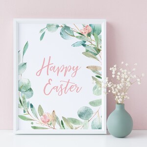 Pu&ograve; includere: Una stampa incorniciata bianca con un'illustrazione ad acquerello di una ghirlanda di foglie di eucalipto e fiori rosa. Il testo "Happy Easter" &egrave; scritto in corsivo rosa all'interno della ghirlanda.