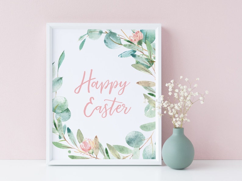 Pu&ograve; includere: Una stampa incorniciata bianca con un'illustrazione ad acquerello di una ghirlanda di foglie di eucalipto e fiori rosa. Il testo "Happy Easter" &egrave; scritto in corsivo rosa all'interno della ghirlanda.