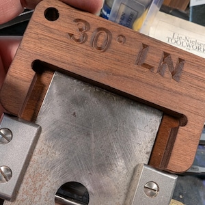 May include: A wooden tool with a metal blade and a 30 degree angle marked on it. The tool is labelled "LN" and has a brass adjustment knob.