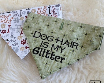 May include: Two triangular pet bandanas. One is light green with a repeating floral pattern and black embroidered text that reads DOG HAIR IS MY GLITTER. The other is white with a repeating pattern of colourful bones, paw prints, and the words woof, bow wow, and sniff.