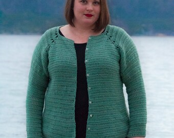 Op de afbeelding: Een groene gehaakte cardigan met knoopsluiting. De cardigan heeft een geribbelde textuur en een licht uitlopende zoom.