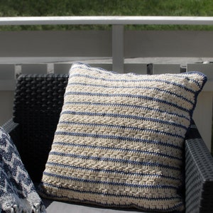 May include: A white and blue striped crocheted pillow on a black wicker chair. The pillow is made with a textured stitch and has a simple, modern design.