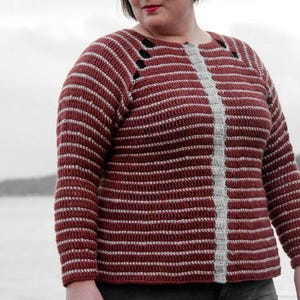 May include: A long-sleeved, horizontally striped sweater in shades of burgundy and white. The sweater features a vertical, light gray stripe down the center and decorative cutouts near the shoulders. The garment is made of a textured, possibly crocheted material.