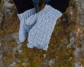 Peut inclure: Une paire de mitaines tricotées bleu clair avec un motif texturé. Les mitaines ont un poignet côtelé noir. Les mitaines sont présentées sur un fond de roche moussue. Conçues pour la chaleur et le confort.