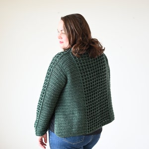 May include: A dark green, hand-crocheted jacket with a textured, open weave design. The jacket features a unique pattern on the sleeves and a boxy silhouette. The garment is shown on a person wearing blue jeans.