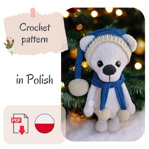 Pode incluir: Um urso de pelúcia branco de crochê usando um chapéu e cachecol azuis com detalhes em creme. O urso tem nariz e olhos pretos. A imagem inclui o texto "Crochet pattern in Polish".