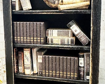 May include: A miniature black wooden bookshelf with five shelves filled with various small books, including sets of dark brown volumes with gold spine details, individual books with illustrated covers, and a small oval framed portrait.