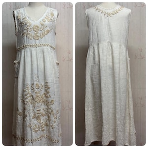 May include: A sleeveless, off-white midi dress made of textured fabric, featuring beige floral embroidery on the bodice, waist, and skirt. The dress includes side pockets and a V-neckline, with a matching floral embroidered detail on the back neckline.