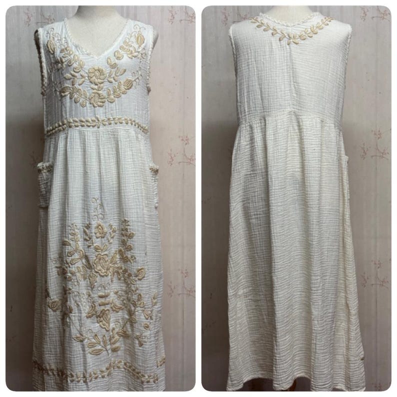 May include: A sleeveless, off-white midi dress made of textured fabric, featuring beige floral embroidery on the bodice, waist, and skirt. The dress includes side pockets and a V-neckline, with a matching floral embroidered detail on the back neckline.