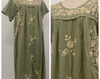 May include: Olive green dress with short sleeves and intricate floral embroidery in cream thread. The dress features a round neckline and vertical embroidered accents, creating a bohemian aesthetic. The dress is displayed on a mannequin.