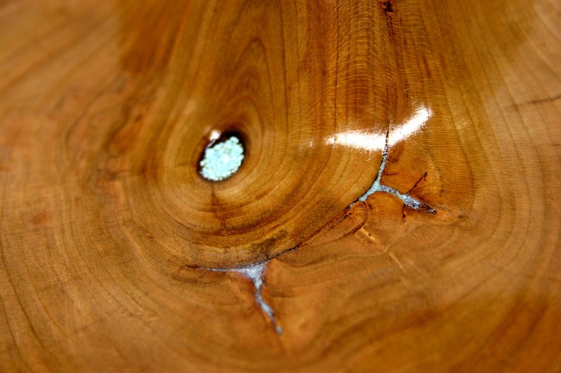 Puede incluir: Primer plano de un cuenco de madera con un patr&oacute;n de veta de madera natural. El cuenco tiene un color marr&oacute;n claro y un acabado liso y pulido. Una peque&ntilde;a incrustaci&oacute;n de resina azul claro es visible en el centro del cuenco.