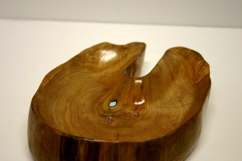 Puede incluir: Un cuenco de madera con una forma natural &uacute;nica y una incrustaci&oacute;n azul claro. El cuenco est&aacute; hecho de una sola pieza de madera y tiene un acabado liso y pulido.