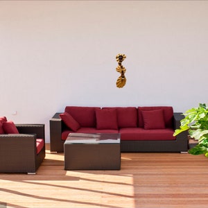 May include: A red wicker sofa with three cushions and a matching wicker armchair with a cushion. The furniture is on a wooden deck with a gold metal wall sculpture hanging on the white wall behind the sofa.