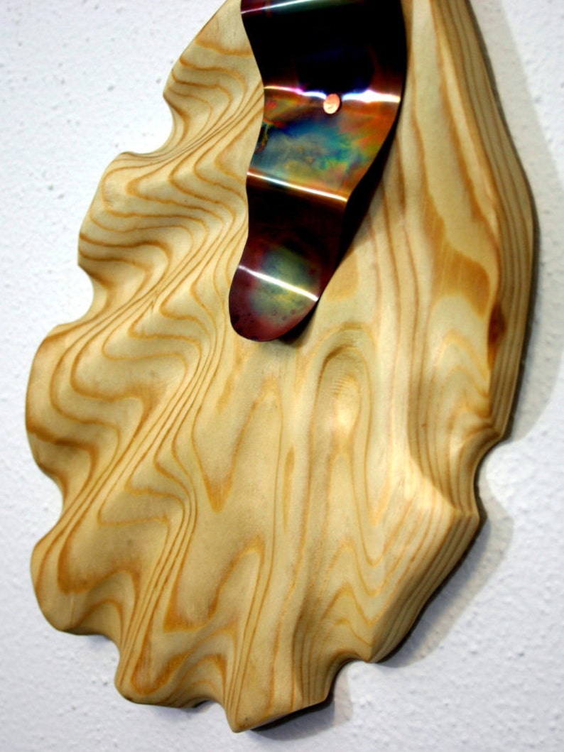 May include: A wooden wall sculpture with a wavy, organic shape. A piece of iridescent metal is attached to the wood, creating a contrasting texture.
