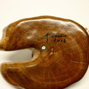 Puede incluir: Una escultura de madera de un pez con una incrustaci&oacute;n de piedra turquesa. La escultura est&aacute; firmada "F.Z. 2016" en la parte inferior.