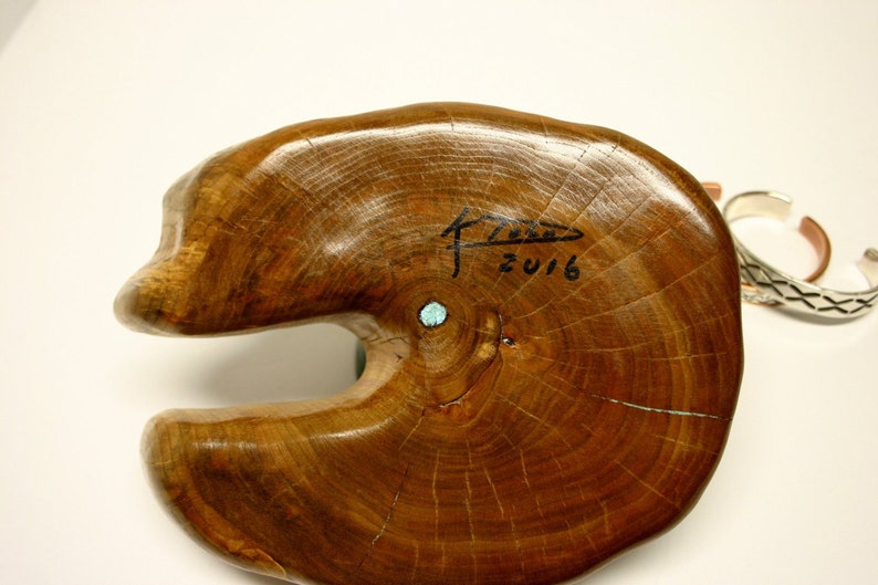 Puede incluir: Una escultura de madera de un pez con una incrustaci&oacute;n de piedra turquesa. La escultura est&aacute; firmada "F.Z. 2016" en la parte inferior.