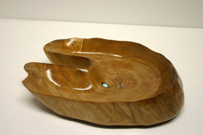 Puede incluir: Un cuenco de madera con una forma &uacute;nica y asim&eacute;trica y un color marr&oacute;n claro. El cuenco tiene un acabado liso y pulido y una peque&ntilde;a incrustaci&oacute;n turquesa.