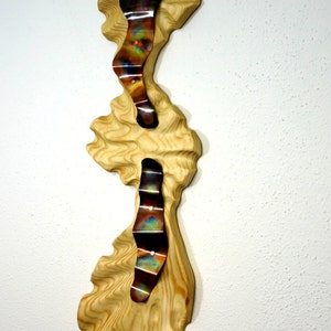 May include: A wall sculpture made of wood and metal. The wood is a light brown color and has a wavy texture. The metal is a copper color and has a shiny finish. The metal is shaped into three wavy lines that are attached to the wood.