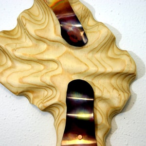 May include: A wooden wall sculpture with a wavy, organic shape. Two pieces of iridescent metal are embedded in the wood, creating a unique and modern design.