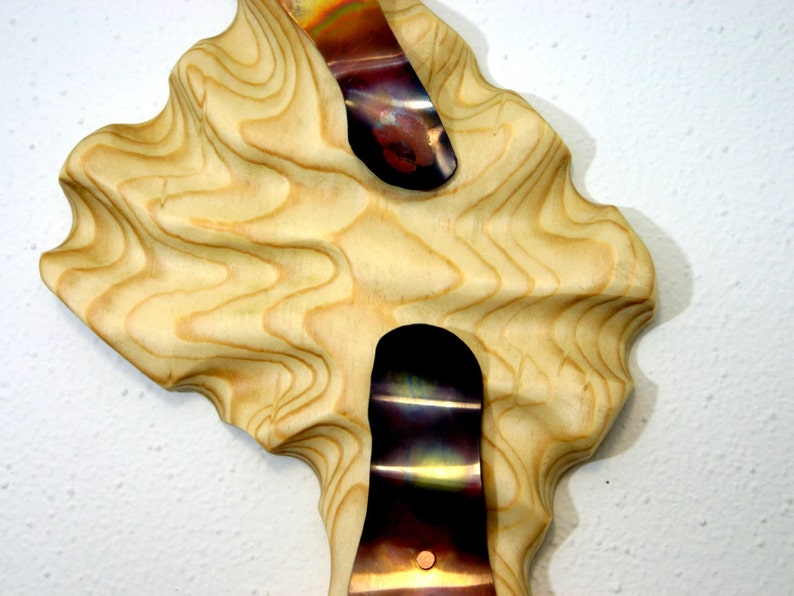 May include: A wooden wall sculpture with a wavy, organic shape. Two pieces of iridescent metal are embedded in the wood, creating a unique and modern design.