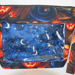 May include: A black zippered Halloween-themed tote bag with a clear plastic window. The bag features a witch's hat, broomsticks, pumpkins, and a starry night sky design. The bag has a brown strap.